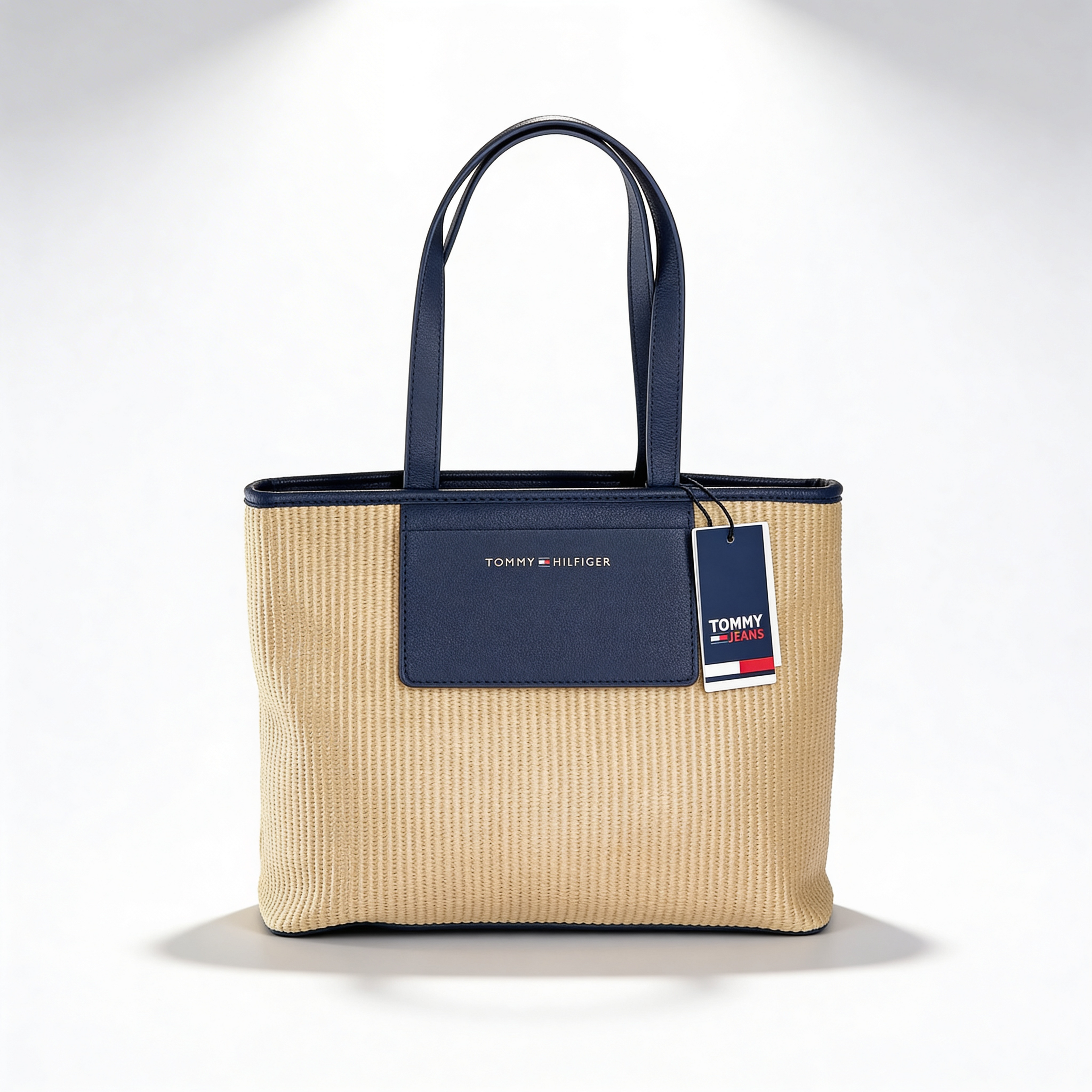 Tommy Hilfiger Iconic Tote, natural canvas with navy leather trim, front view with TOMMY HILFIGER plaque and flag hangtag