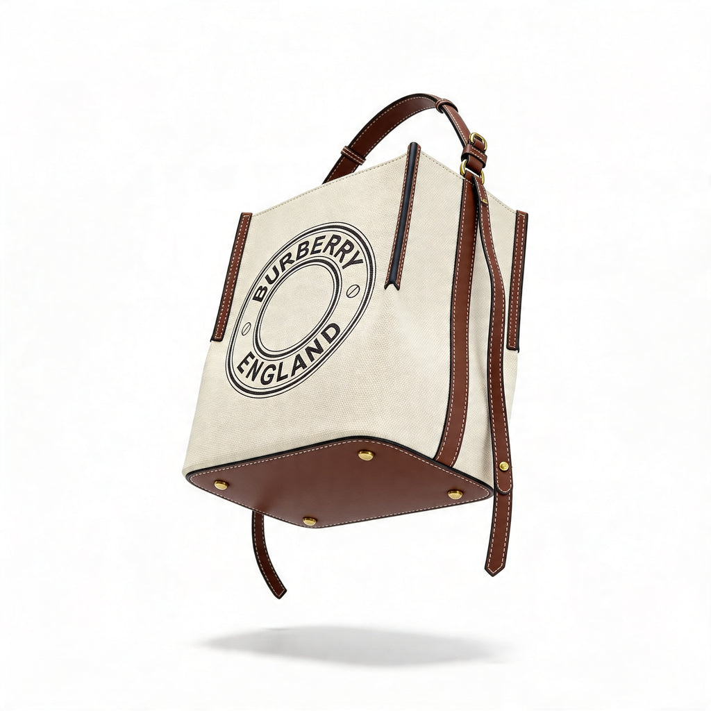 Burberry Logo Graphic Small Canvas Tote, natural canvas with tan leather trim, floating composition showing reinforced leather base and shoulder strap
