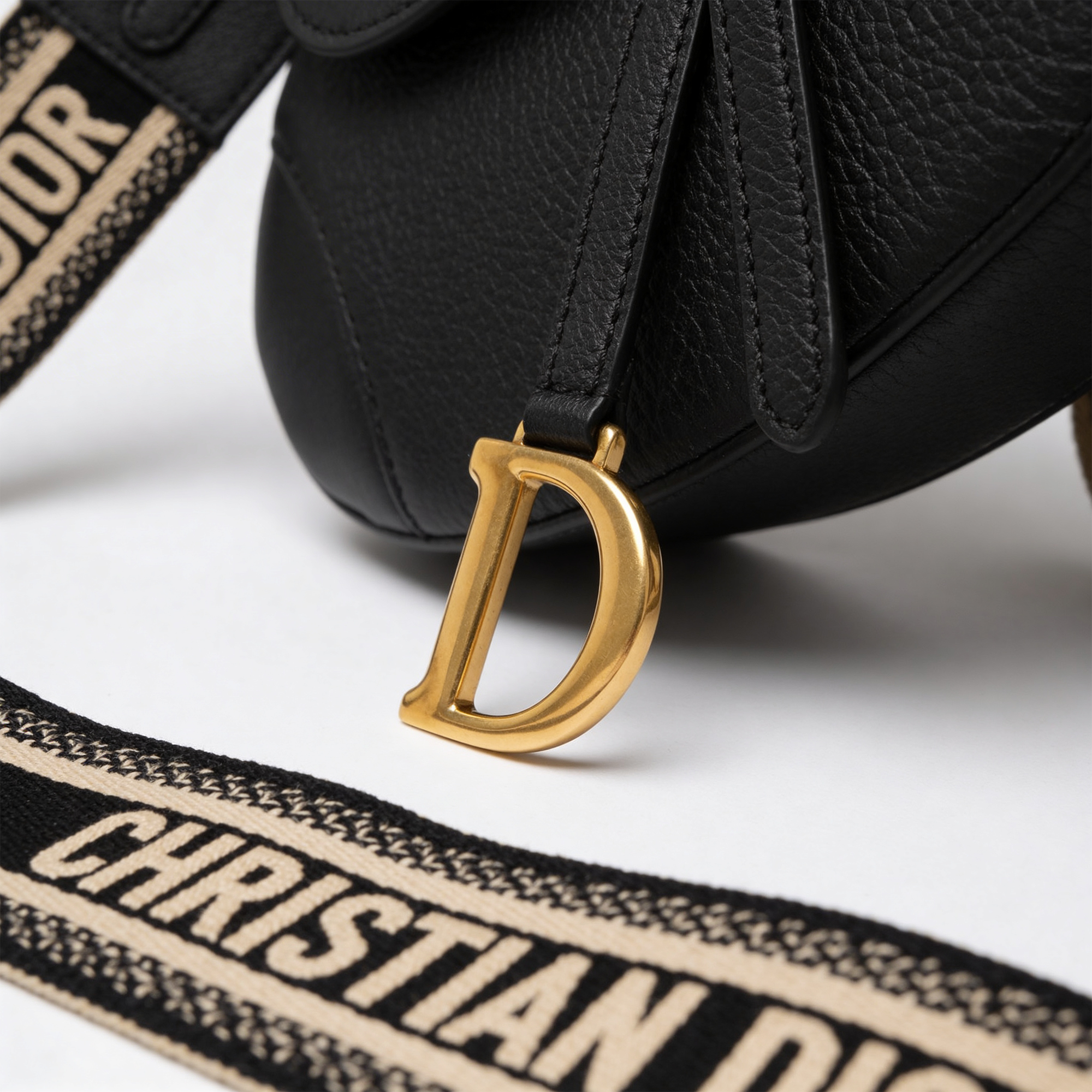 Close-up of gold D-charm hardware and embroidered Christian Dior strap on black grained leather Saddle Bag